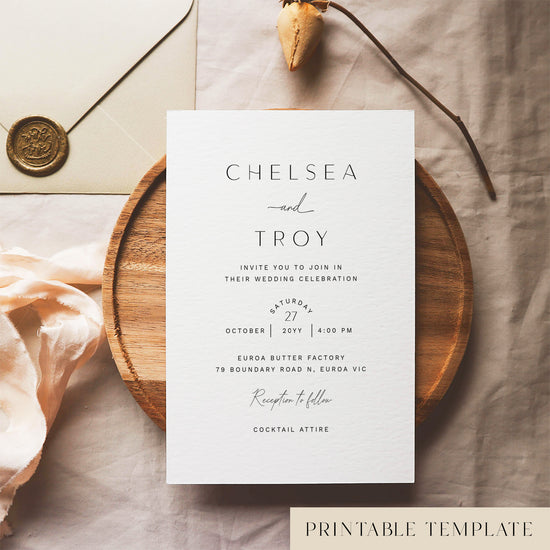 Wedding invitation template design on a white card sitting on a wooden plate with decorative elements.