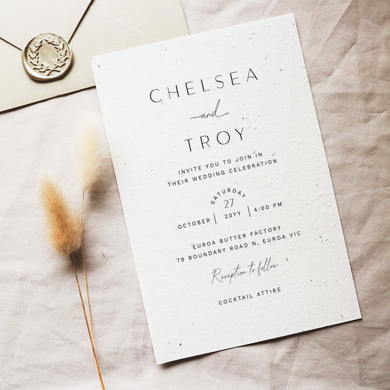 Wedding invitation card on textured card with envelope on fabric background.