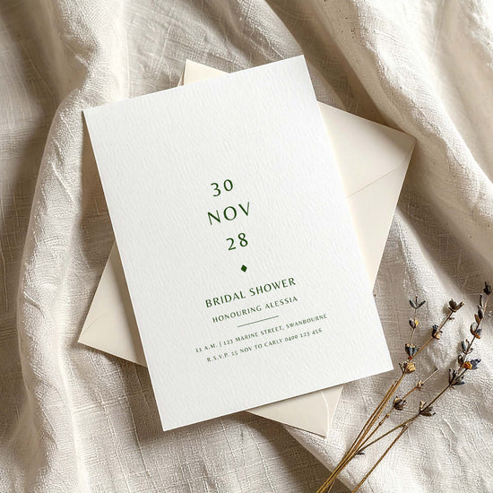 Minimal bridal shower invitation on textured card with envelope on fabric background.