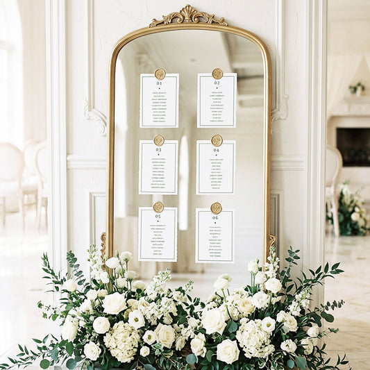 Wedding mirror table plan display with six printable green and white table cards attached with gold wax seals in an elegant light-filled wedding ballroom setting.