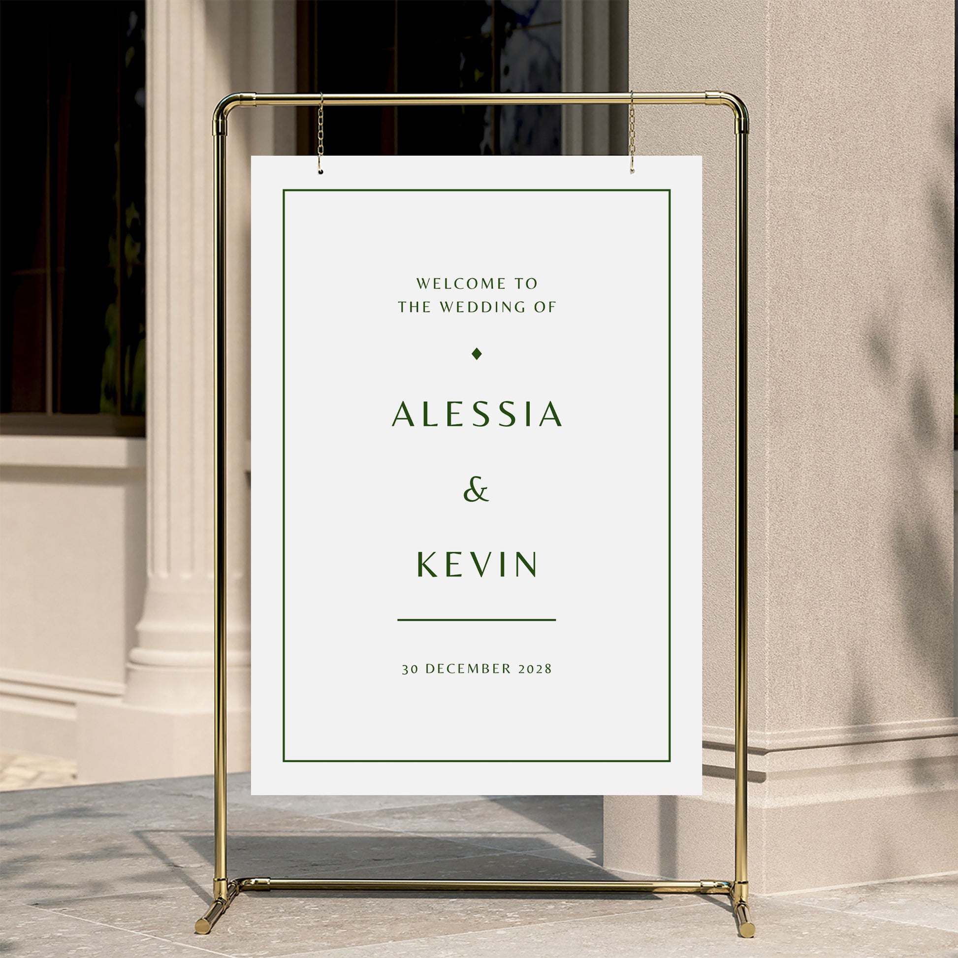 Minimal welcome sign for a wedding with a gold stand against a neutral wall.