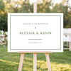 Horizontal wedding welcome sign on an easel with a blurred outdoor ceremony background.