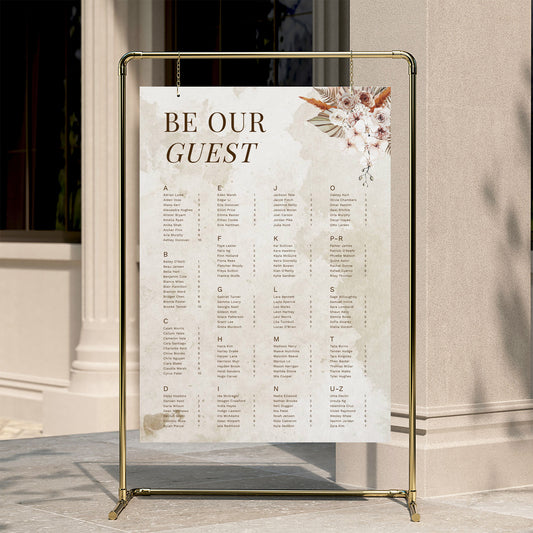 Alphabetical wedding seating chart template displayed on a gold stand against a neutral wall.