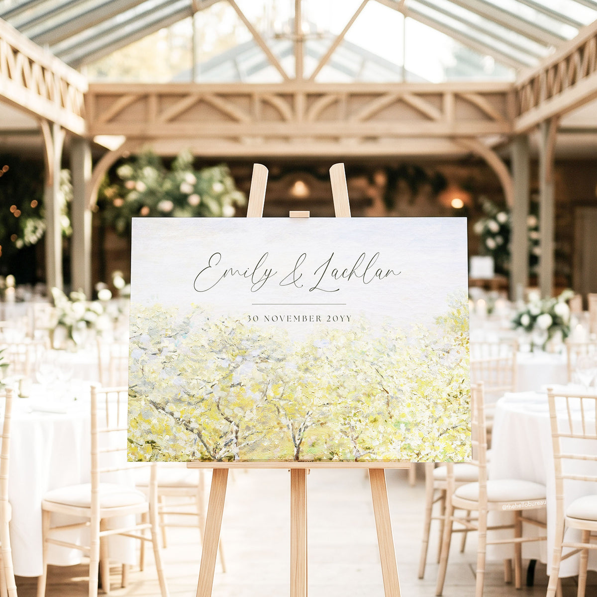 Pastel garden Monet wedding sign on a wooden easel in a light-filled glass conservatory, surrounded by white chairs and soft green florals.