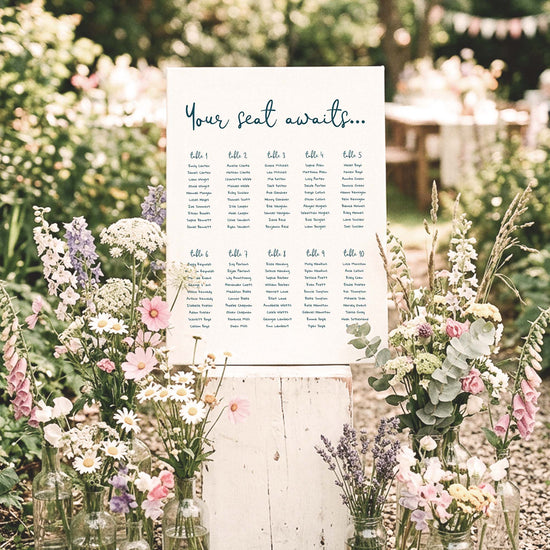 DIY whimsical 10-table wedding seating chart template styled at an outdoor wedding surrounded by wildflowers and greenery.