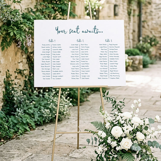 Printable 3 long tables wedding seating chart template displayed on a gold easel at an outdoor garden wedding venue.
