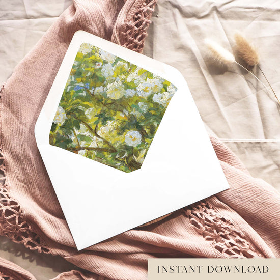 Printable white roses envelope liner for 5x7 wedding invitations, with painted white garden roses among lime and olive green leaves, shown inside a white envelope on dusty pink fabric.
